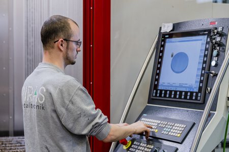 Das Hedelius 4-/5-Achs-Bearbeitungszentrum Tiltenta 7-3600, das für seine Flexibilität und Präzision bekannt ist. Die Maschine verfügt über eine innovative 2-Spindel-Technologie, die es ermöglicht, komplexe Werkstücke effizient und genau zu bearbeiten. Das Bild zeigt die hochentwickelte Maschine in Betrieb, mit sichtbaren Bedienelementen und Werkzeugen, die ihre Vielseitigkeit und technologische Fortschrittlichkeit unterstreichen. Im Fokus steht dabei ein Anwender an der Maschinensteuerung.