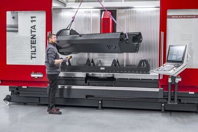 Die Einsatzmöglichkeiten der HEDELIUS Bearbeitungszentren. Das 4-/5-Achs-Bearbeitungszentrum TILTENTA 11 wird mit einem schweren, langen Werkstück per Kran von einem Anwendungstechniker beladen. Die langen Verfahrwege und der große Maschineninnenraum ermöglichen somit die Bearbeitung von Teilen mit besonderen Anforderungen.