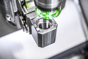 Abbildung des bidirektionalen Tasters m&h IRP 25.50. Eingesetzt wird er Taster an einem eingespannten Werkstück zur präziseren Bearbeitung.