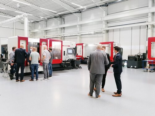 Besucher der Hausaustellung befinden isch im Technologiezentrum und schauen sich die ausgestellten HEDELIUS Bearbeitungszentren an. Zu sehen ist eine ACURA mit MARATHON Automation und im Hintergrund steht die TILTENTA 7