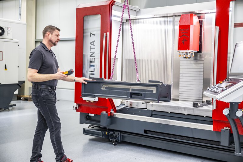 CNC 4-/5-Achs-Bearbeitungszentrum wird mit Kran beladen. Langes, schweres Werkstück wird eingesetzt.