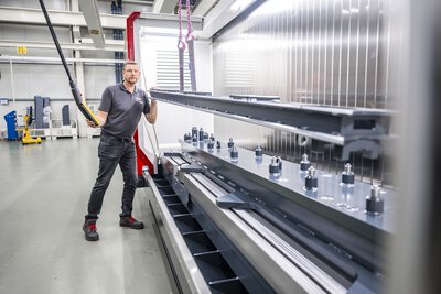 5-Achs-CNC-Bearbeitungszentrum TILTENTA 7-3600 NEO mit Schwenkspindel während der Kranbeladung eines Bauteils durch den Bediener