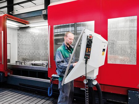 Bild des HEDELIUS 4-/5-Achs-Bearbeitungszentrums TILTENTA-7-4200 in der Produktionshalle des Kunden. Sichtbar ist der große Verfahrweg der X-Achse und ein Anwender an der Maschinensteuerung. Dank großer Verfahrwege und einer stufenlos schwenkbaren Hauptspindel können unterschiedlichste Werkstücke verarbeitet werden.